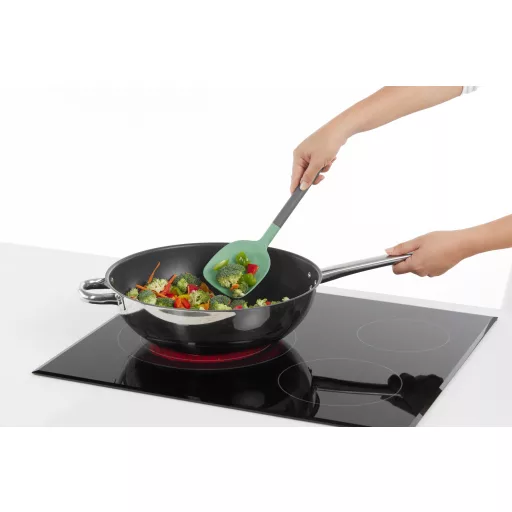 A zöld színű műanyag spatula széles, kúpos fejrésze tökéletesen leköveti a wok serpenyők íves belső formáját, biztosítva az alapanyagok hatékony és karcolásmentes forgatását a mé